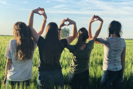 Gruppe von Mädchen in einem Feld, die mit ihren Händen zusammen Herzen formen